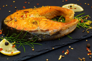 Grilled salmon. A piece of fried fish on a black slate tray. Served with lemon wedges and spices - 425803502