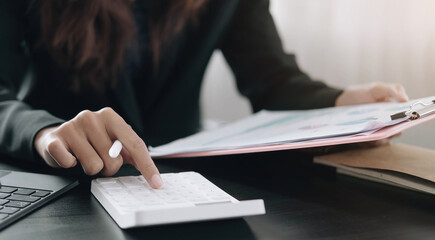 Close up Business woman using calculator and laptop for do math finance on wooden desk in office and business working background, tax, accounting, statistics and analytic research concept