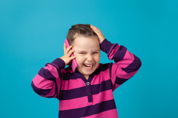 close-up portrait of a laughing, cheerful, positive girl with pigtails making a phone call and holding her head with her hand isolated on a blue background.