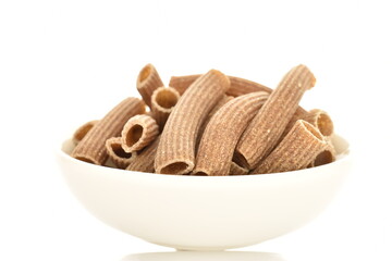 Dark brown, uncooked, organic rye pasta in a white ceramic bowl , close-up isolated on white.