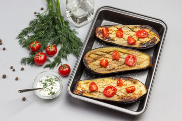 Fototapeta na wymiar Grilled baked eggplant with tomatoes in pallet. Dill and tomatoes on table. Sauce in glass bowl