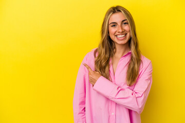 Fototapeta premium Young blonde caucasian woman isolated on yellow background smiling and pointing aside, showing something at blank space.