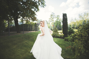 Beautiful bride in elegant white dress holding bouquet posing in park
