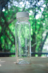 Selective focus image of empty plastic bottle with white lid, water drops in glass