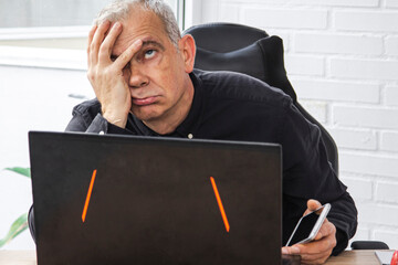 stressed or overwhelmed man in office with laptop and mobile phone