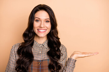 Portrait of charming cheerful wavy-haired girl holding on palm copy empty blank place space isolated over beige pastel color background