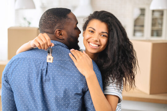 Close photo of delighted couple who bought new flat, black man standing with his back and hugging his happy wife with the keys to their new apartment, buying a property, a new stage in a relationship