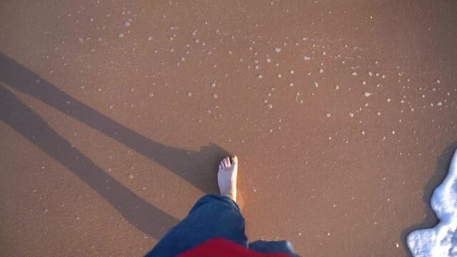 vista de pies de un chico caminando en la arena con el mar al lado