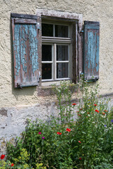 Altes Fenster mit verwitterten Fensterläden aus Holz und einem Blumenbeet
