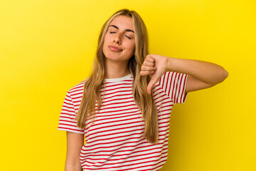 Young blonde caucasian woman isolated on yellow background showing a dislike gesture, thumbs down. Disagreement concept.