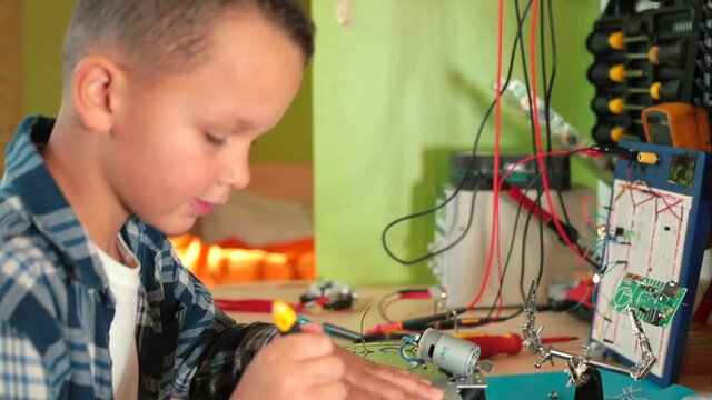 A boy in a workshop unscrews the screw on a toy car. He turns with his hand, remanufactures the wheel. Make a toy with your own hands. Favorite hobby.