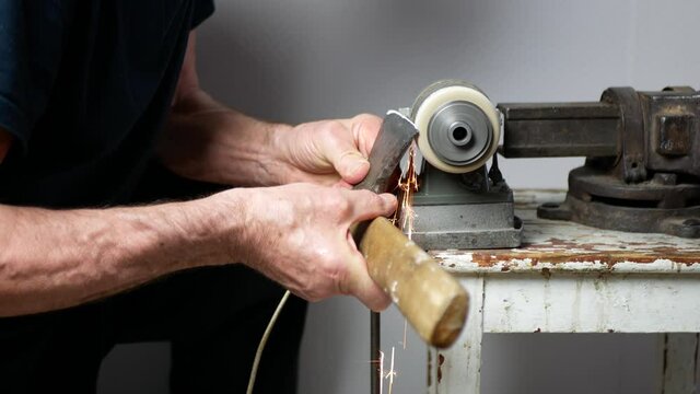 Old axe restoration. Man is sharpening an ax with an electrical grinding machine