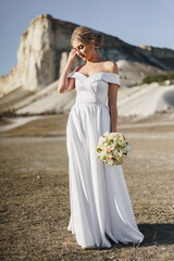 Fototapeta na wymiar Beautiful bride in a wedding dress with a bouquet standing against white rock