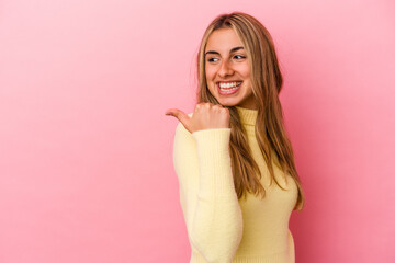 Young blonde caucasian woman isolated on pink background points with thumb finger away, laughing and carefree.