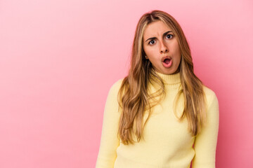 Young blonde caucasian woman isolated on pink background being shocked because of something she has seen.