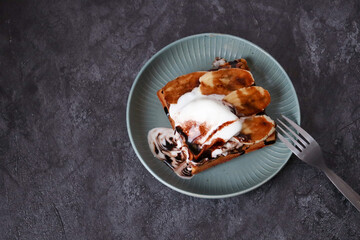Belgian Waffle with chocolate cream and banana slices and ice cream in a plate on dark background, close up, horizontal, copyspace