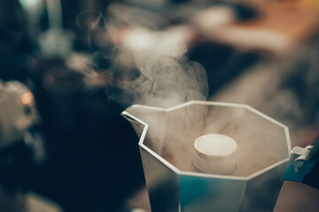 Brewing black moka coffee using moka coffee maker and boiling with smoke on gas stove.