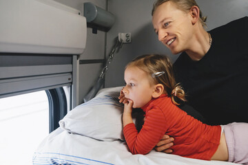 Father with child travalling in the train, having fun enjoying scene through window while riding on railroad togather in sleeping car