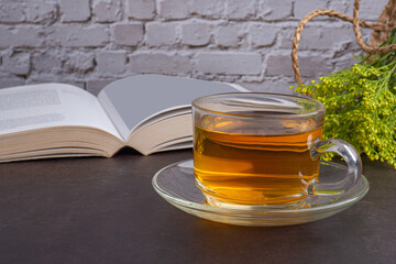 A teacup with flowers and a book placed on a dark background with a white brick wall. Space for text. Morning beverage and relaxation concept