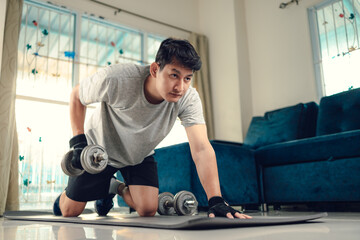 Fototapeta na wymiar Young man doing exercises triceps muscle with dumbbell on yoga mat in living room at home. Fitness, workout and traning at home concept.