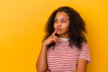 Fototapeta na wymiar Young african american woman isolated on yellow background looking sideways with doubtful and skeptical expression.