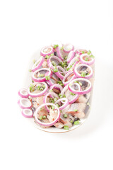 Salted herring with rings of red onion rings on oval plate on a light background . Marinated sliced fish. Traditional russian appetizer