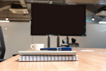 Close up pen and notebook on table with blank display television in meeting room