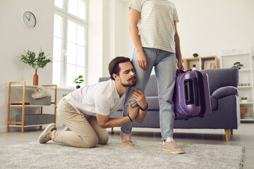 Young married couple breaking up. Angry woman leaving home with packed suitcase. Clingy desperate...