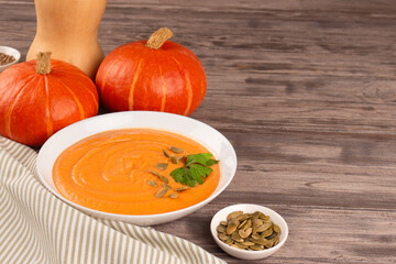 Pumpkin cream soup in white bowl toped with parsley and pumpkin seeds on wooden table background with copy space for text. Vegan food concept, homemade soup recipe. Selective focus