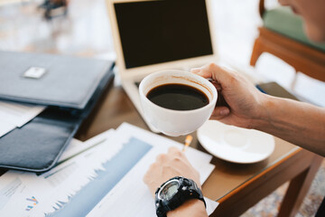 businessman holding coffee cup in hands and computer on table in coffee shop. Young freelancer drink coffee and working.