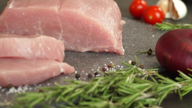 Camera movement of fresh sliced steak pork on background of vegetables, greens and spices. Food concept, cooking meat, loin, carbonate.
