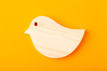 A figurine of a bird carved from solid pine by a hand jigsaw. On a yellow background