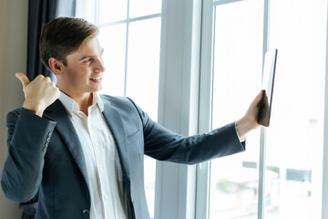 Happy Young business man using digital tablet for video conference to colleague in office at company near window Handsome guy wear suit and shirt He get satisfied Business and technology concept