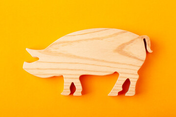 A figurine of a pig carved from solid pine by a hand jigsaw. On a yellow background