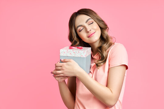 Happy woman holding and hug gift box on pink background.