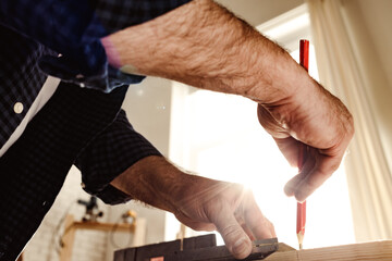 Carpenter makes pencil marks on a wood plank