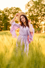 Fototapeta na wymiar Stylish girl in violet dress and hat in field. Happy young woman on the sunset or sunrise in summer nature. Fashion and lifestyle concept.