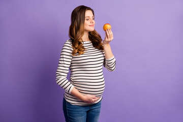 Photo of pretty dreamy lady waiting baby dressed striped shirt arm tummy enjoy fruit aroma isolated violet color background