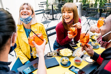 Multiracial friends wearing face masks drinking cocktails at bar restaurant - New normal friendship...