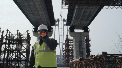 Male engineer walking and talking under bridge
