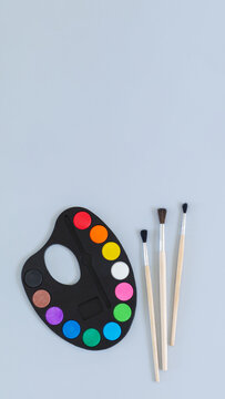 Art palette with paint and paintbrushes top view on gray background
