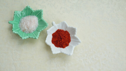 Pink Himalayan salt and red hot chili powder in small leaf shaped dishes, placed on a white textured board..