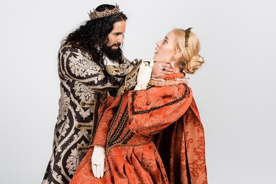 cruel hispanic king in medieval clothing choking shocked queen in golden crown isolated on white