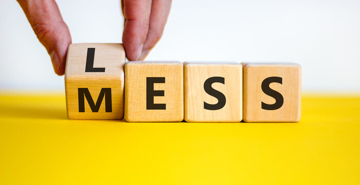 Less mess symbol. Businessman turns the cube and changes the word 'mess' to 'less'. Beautiful yellow table, white background, copy space. Business and less mess concept.