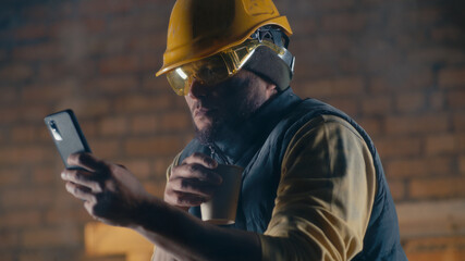 Male builder with hot drink using smartphone