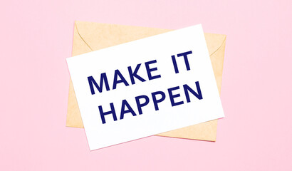 On a light pink background - a craft envelope. It has a white sheet of paper that says MAKE IT HAPPEN.