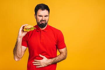 Young man holding a piece of sandwich. Student eats fast food. Burger is not helpful food. Very hungry guy. Diet concept. Isolated over yellow background.