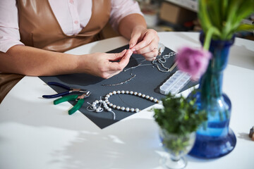 Naklejka premium Skilled female jeweler stringing beads at the table