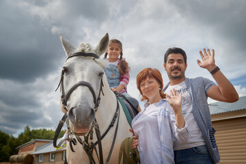 Kirov, Russia - August 07, 2020: A family including a mother, father and daughter walks and rides a horse in nature among green trees. Man, woman, girl with horse in nature in summer