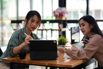 Two young Asian businesswoman brainstorm and analyze project using a tablet at the office.